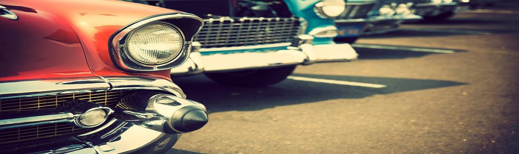 A zoomed in view of a row of vintage cars with only their front bumpers and wheels showing
