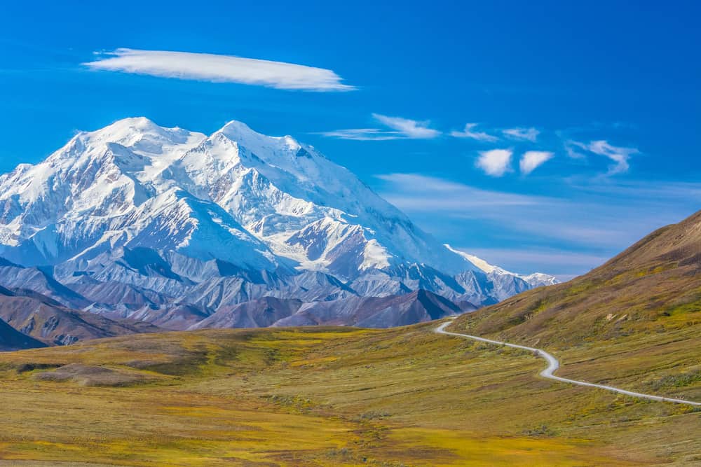 Rolling hills and a winding road set in round of snow-capped mountains in Denali National Park. 