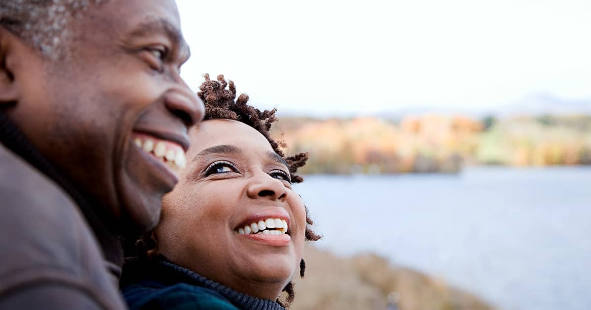 A smiling senior couple overlook the water while on vacation.