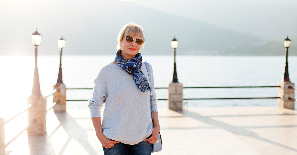 Solo senior woman enjoys her solo trip while standing on a pier.