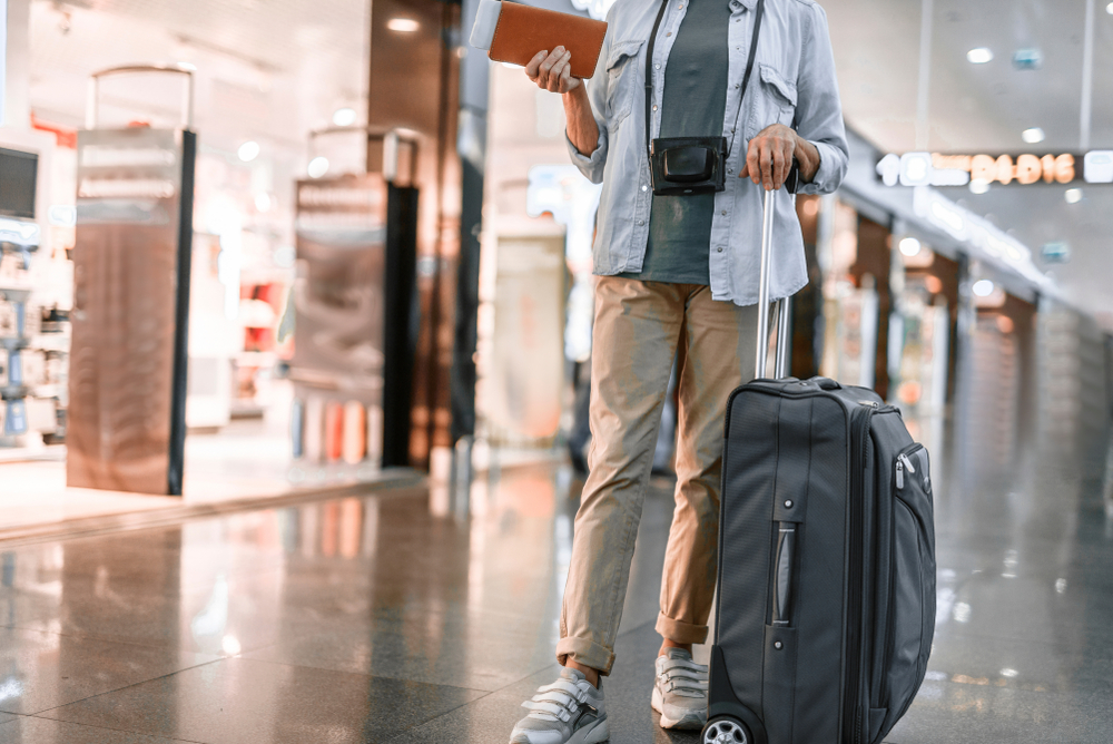 senior woman traveling in airport with suitcase and camera