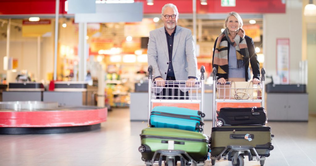 happy senior couple walking through the airport while traveling with luggage carts