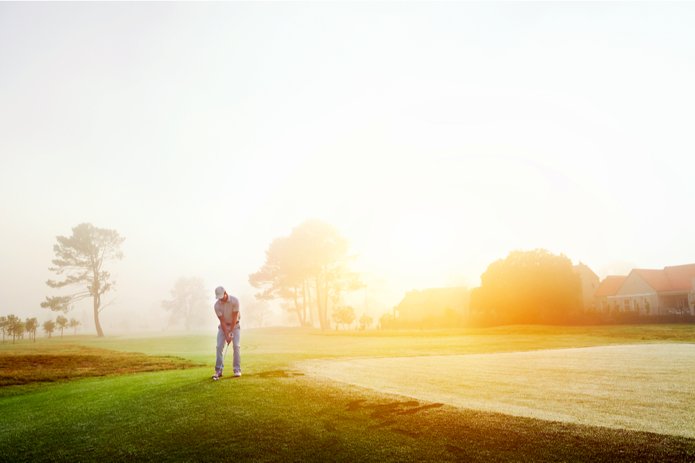 Golfer chipping onto the green at sunrise on the golf course in misty condition