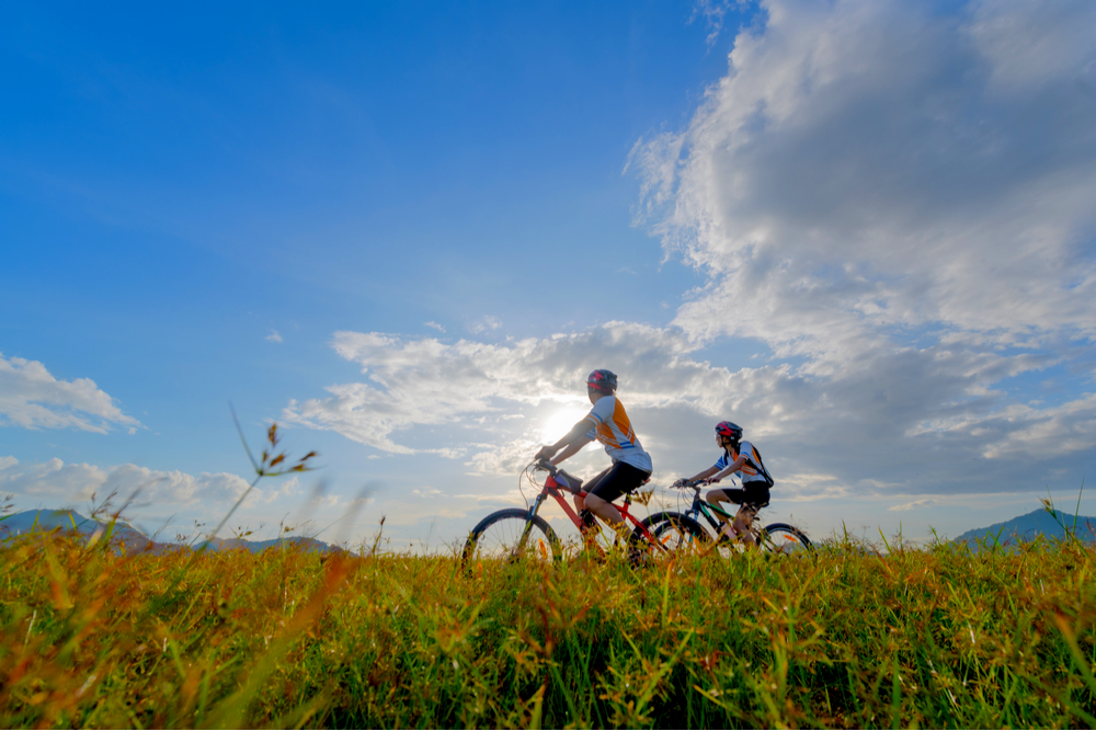 senior couple riding bikes through the grass on sunny day