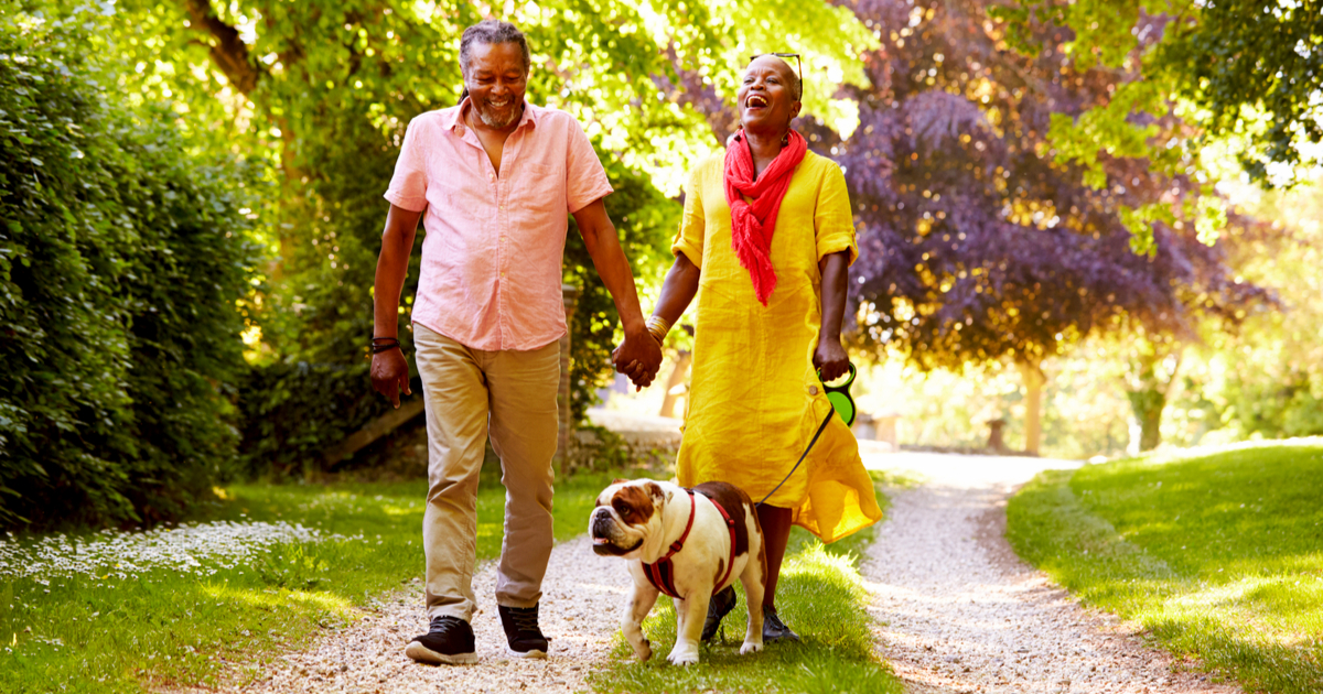 Senior Couple Walking With Pet Bulldog In Countryside